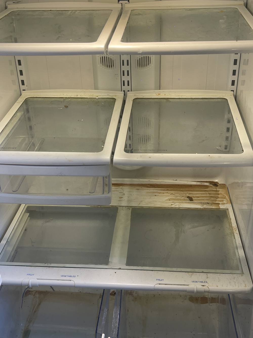 Refrigerator interior before cleaning, with stained shelves and spill residue